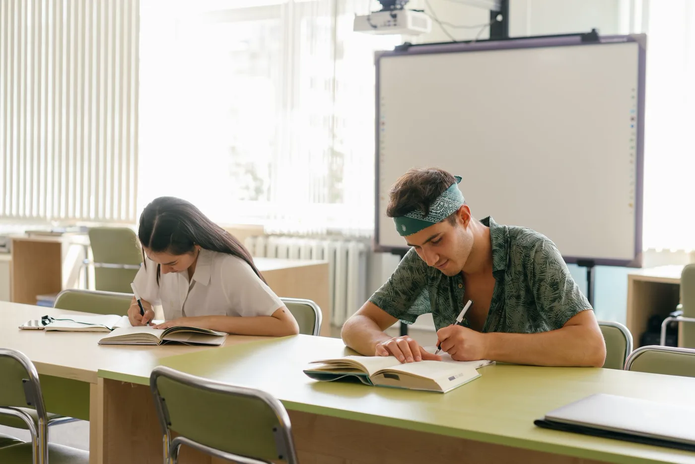 Dos estudiantes resuelven ejercicios en sus libros dentro de un aula iluminada