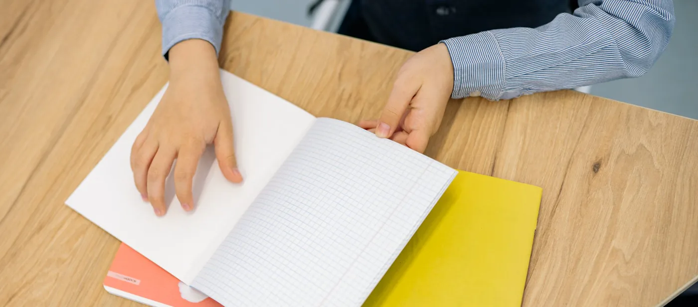 Manos abriendo un cuaderno cuadriculado sobre una mesa de madera
