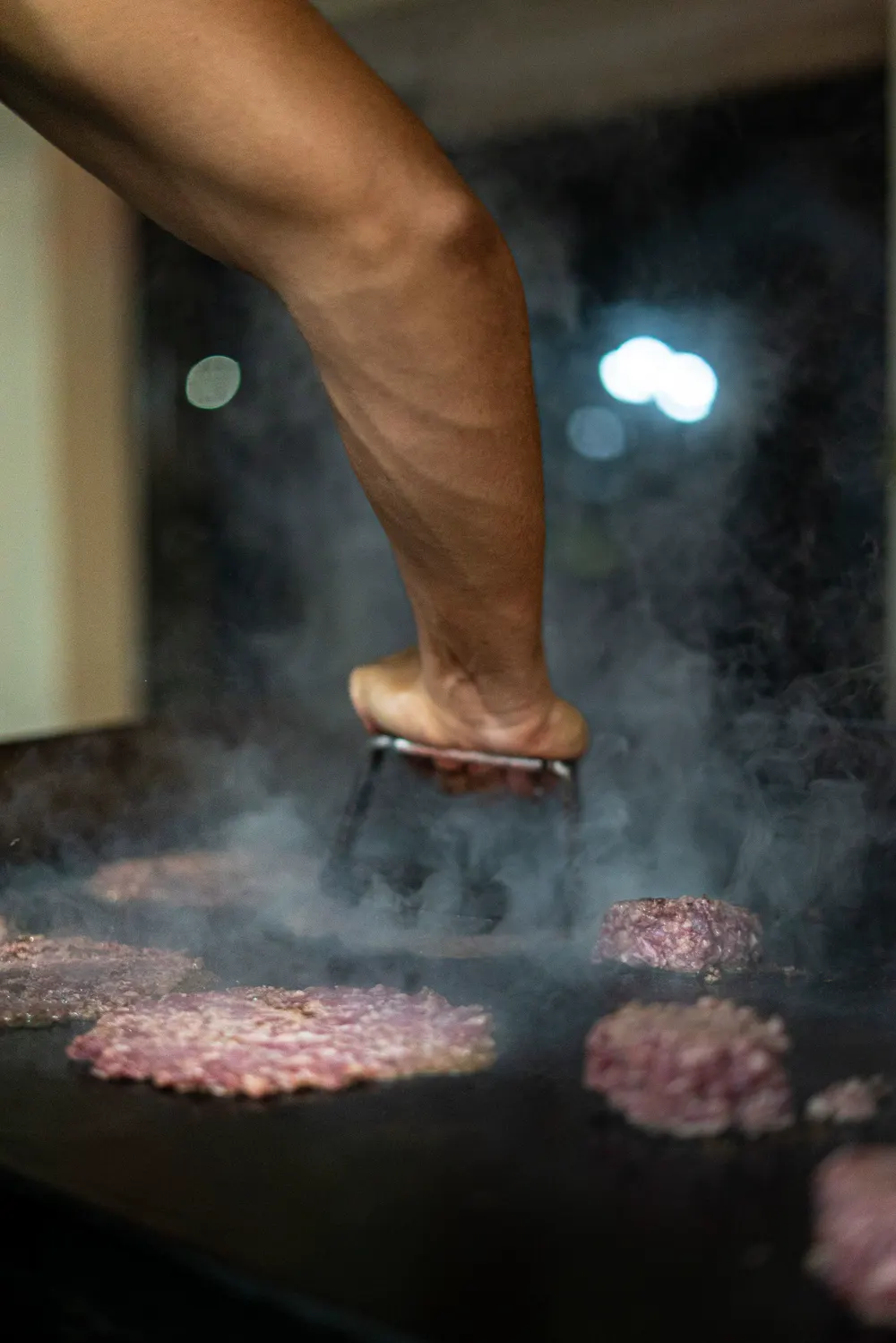 Cocinero aplastando bolitas de carne sobre la plancha con humo