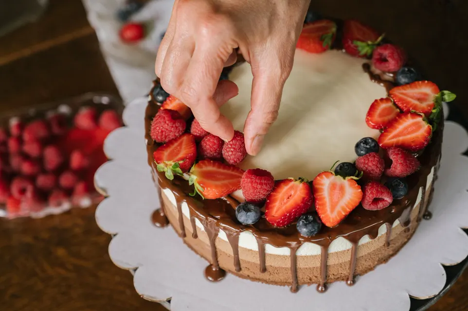 Manos colocando fresas sobre una torta con ganache